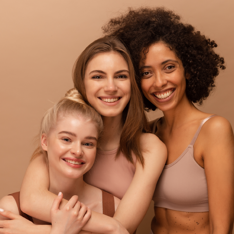 Three women posing together against a beige background
